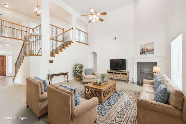 living room with light carpet, a towering ceiling, ceiling fan with notable chandelier, and a tile fireplace