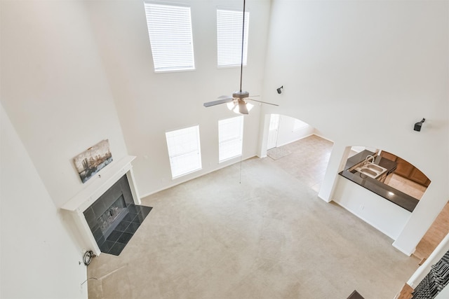 unfurnished living room featuring a tile fireplace, a towering ceiling, light carpet, and ceiling fan