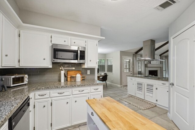 kitchen featuring decorative backsplash, light stone countertops, white cabinetry, island exhaust hood, and stainless steel appliances