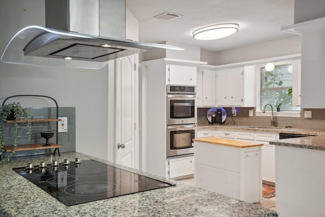 kitchen featuring white cabinetry, sink, stainless steel double oven, light stone counters, and black electric stovetop