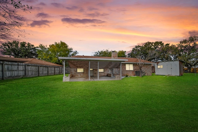 back house at dusk with a lawn, a shed, and a patio