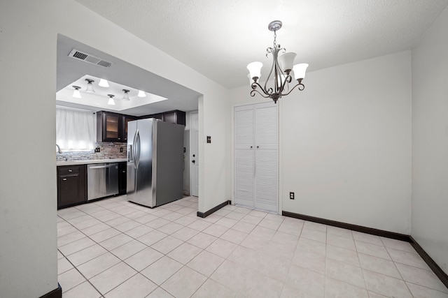 kitchen featuring backsplash, dark brown cabinetry, stainless steel appliances, an inviting chandelier, and hanging light fixtures