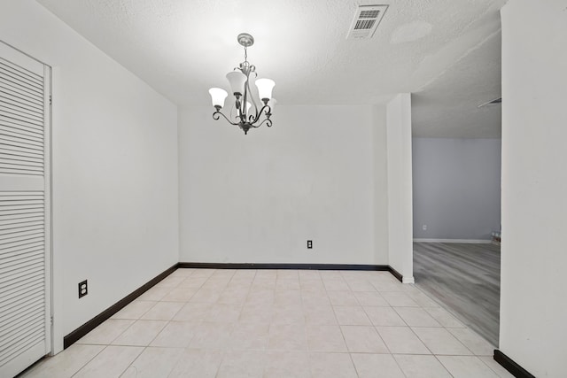 tiled spare room with a notable chandelier and a textured ceiling