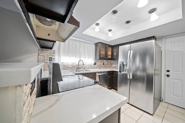 kitchen featuring sink, light stone countertops, light tile patterned floors, appliances with stainless steel finishes, and a tray ceiling