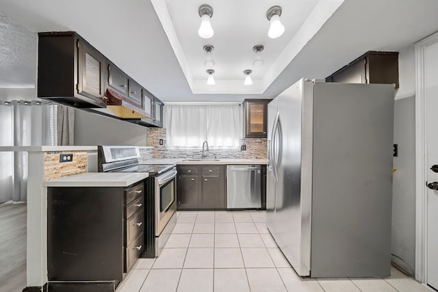 kitchen featuring appliances with stainless steel finishes, tasteful backsplash, a tray ceiling, sink, and light tile patterned flooring