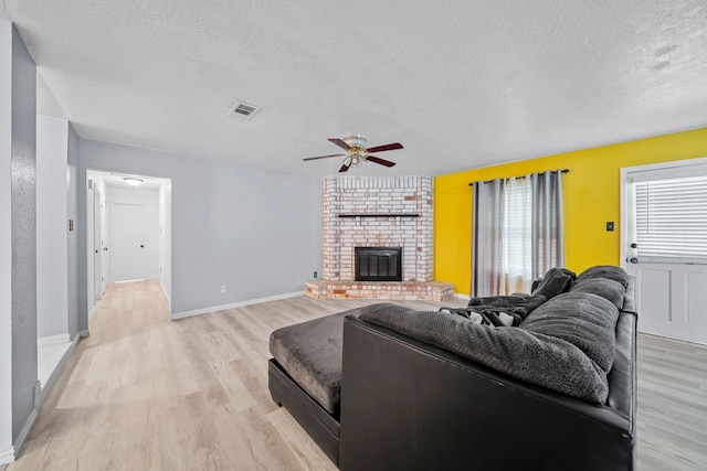 living room featuring ceiling fan, a fireplace, light hardwood / wood-style floors, and a textured ceiling