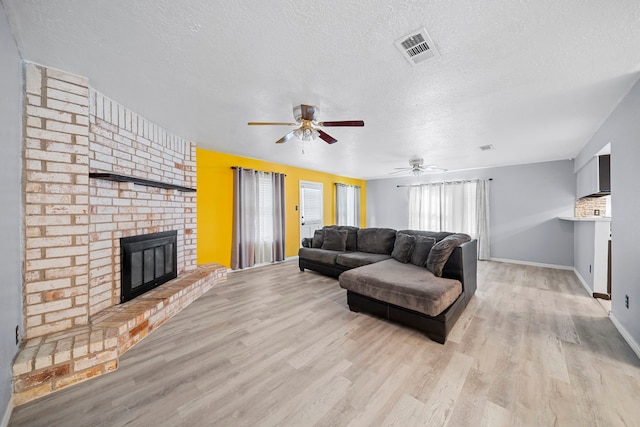 living room with a fireplace, a textured ceiling, light hardwood / wood-style flooring, and ceiling fan