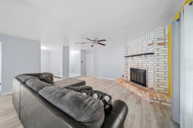 living room with a brick fireplace, ceiling fan, a textured ceiling, and light wood-type flooring