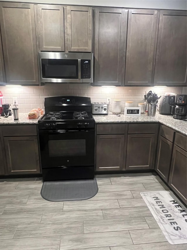 kitchen featuring dark brown cabinets, black gas stove, light stone countertops, and decorative backsplash