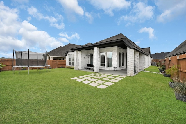 back of property featuring a patio area, a trampoline, and a yard