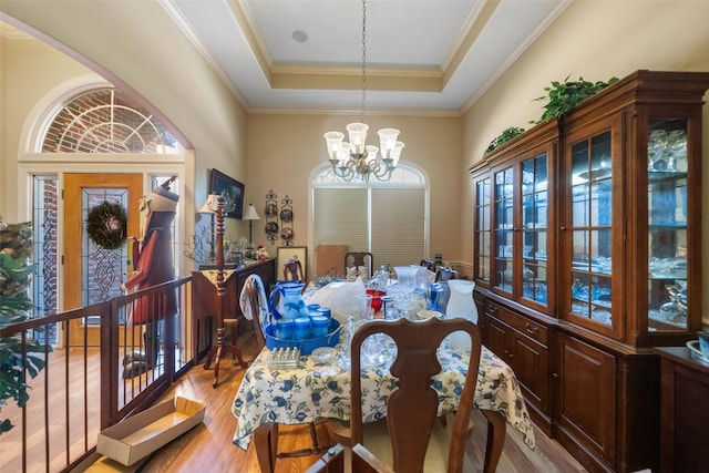 dining room featuring light hardwood / wood-style floors, a raised ceiling, a notable chandelier, and crown molding