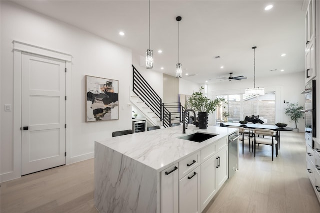 kitchen featuring white cabinets, light stone countertops, a kitchen island with sink, and sink