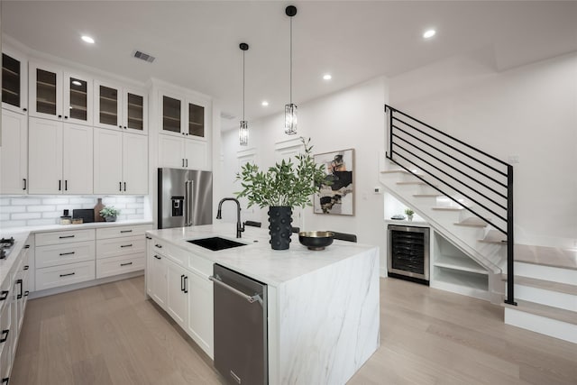 kitchen featuring appliances with stainless steel finishes, a kitchen island with sink, beverage cooler, sink, and white cabinetry