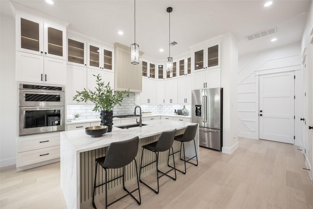 kitchen featuring light wood-type flooring, stainless steel appliances, tasteful backsplash, and a center island with sink