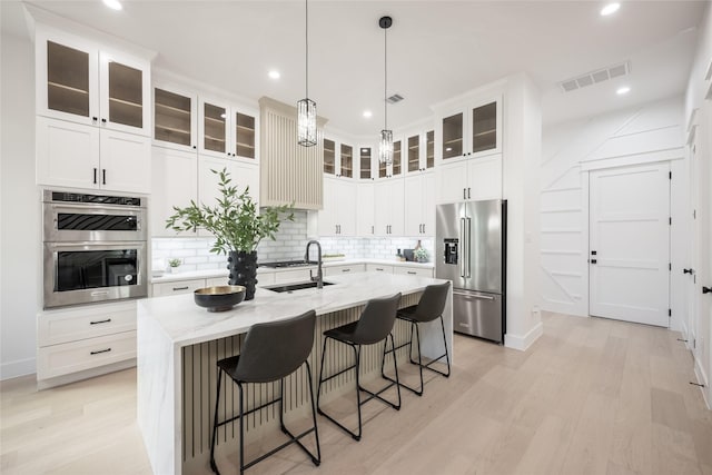 kitchen featuring backsplash, sink, stainless steel appliances, and an island with sink