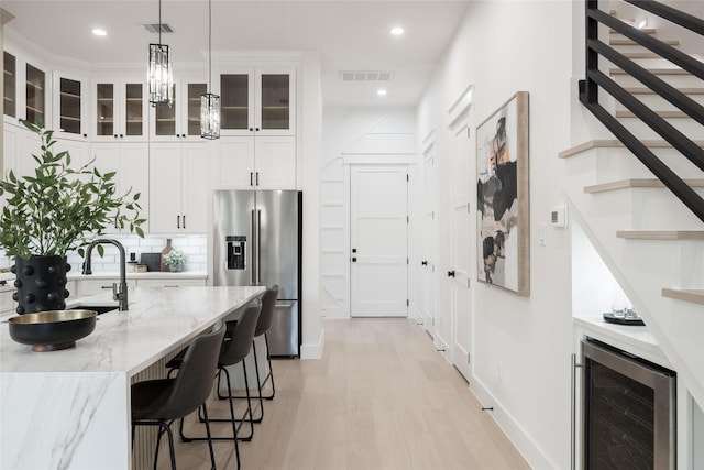 kitchen featuring beverage cooler, tasteful backsplash, light stone counters, high quality fridge, and light wood-type flooring