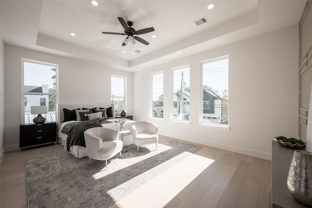 bedroom featuring multiple windows, hardwood / wood-style flooring, a raised ceiling, and ceiling fan