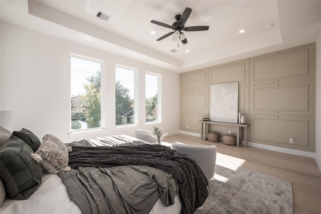 bedroom with a raised ceiling, ceiling fan, and light hardwood / wood-style floors