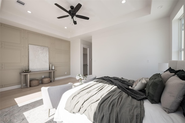 bedroom featuring ceiling fan, light wood-type flooring, and a tray ceiling