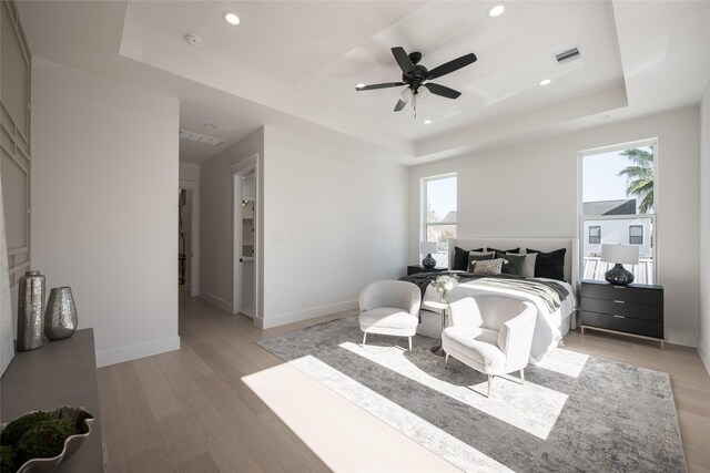 bedroom featuring multiple windows, wood-type flooring, a raised ceiling, and ceiling fan