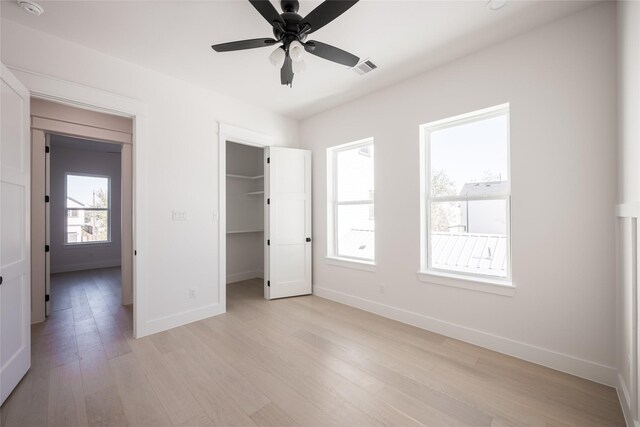 unfurnished bedroom with a walk in closet, ceiling fan, a closet, and light hardwood / wood-style floors