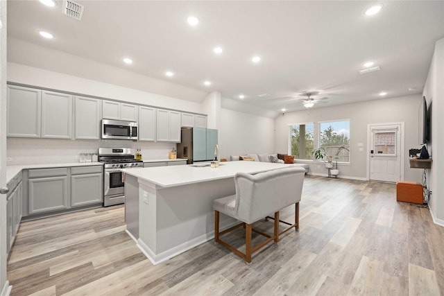 kitchen featuring appliances with stainless steel finishes, gray cabinetry, ceiling fan, light hardwood / wood-style flooring, and an island with sink