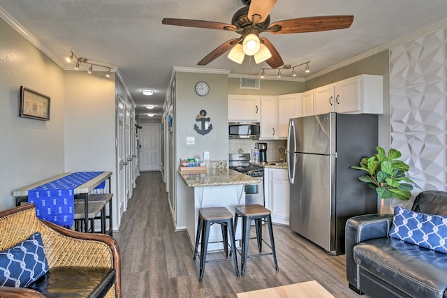 kitchen featuring white cabinets, appliances with stainless steel finishes, light stone counters, and crown molding