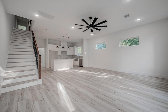 unfurnished living room featuring a ceiling fan, visible vents, stairway, and light wood-type flooring