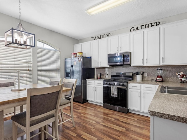 kitchen with dark wood-type flooring, white cabinets, sink, decorative light fixtures, and stainless steel appliances