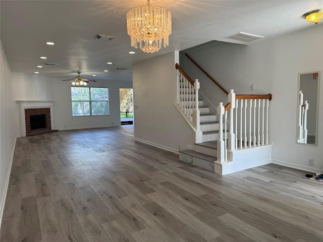 unfurnished living room featuring a textured ceiling, a fireplace, wood-type flooring, and ceiling fan with notable chandelier