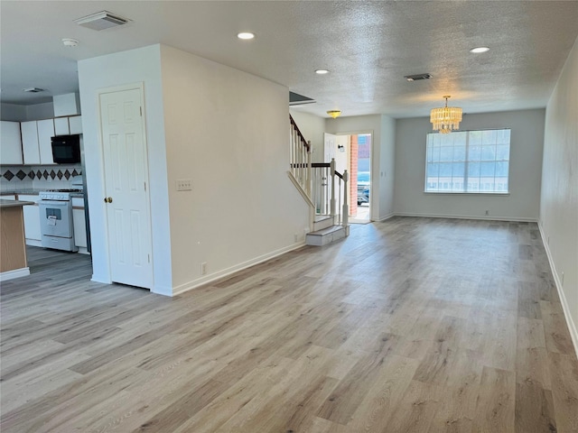 unfurnished living room featuring a chandelier, a textured ceiling, and light hardwood / wood-style floors