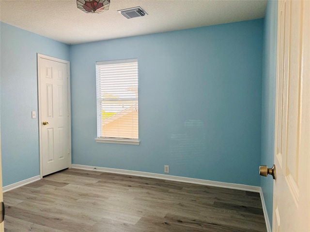 spare room with a textured ceiling and light hardwood / wood-style flooring