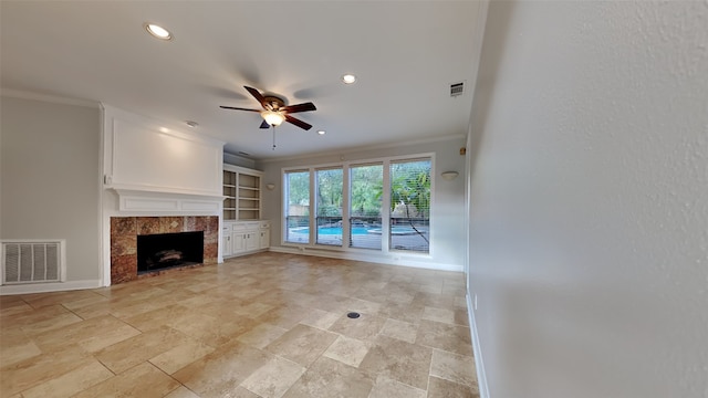 unfurnished living room featuring built in features, ceiling fan, crown molding, and a tiled fireplace