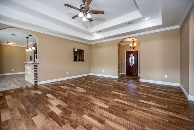 unfurnished living room with a raised ceiling, crown molding, dark wood-type flooring, and ceiling fan with notable chandelier