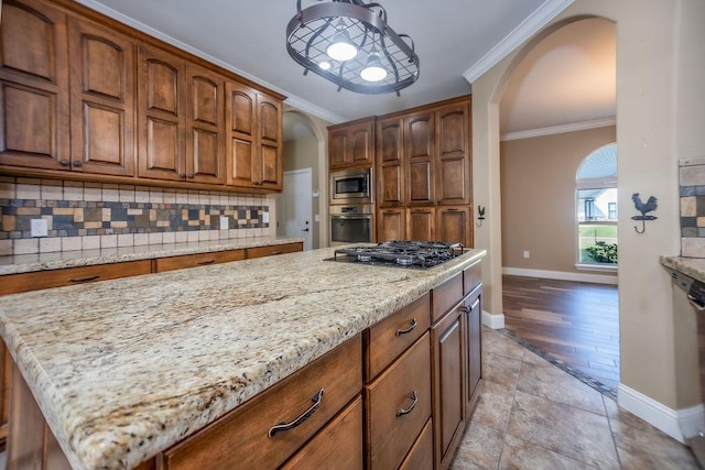 kitchen with light stone counters, crown molding, appliances with stainless steel finishes, a kitchen island, and decorative backsplash