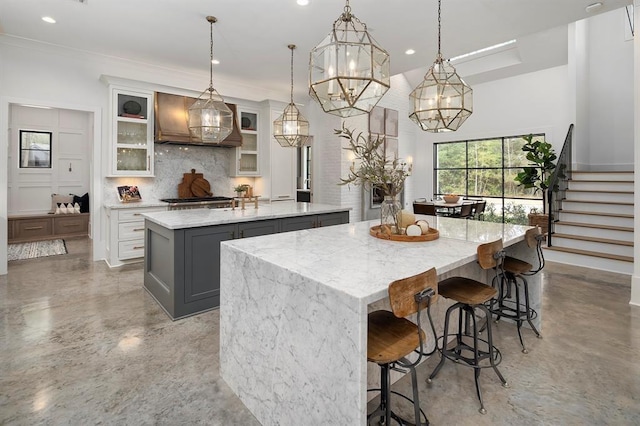 kitchen with a center island with sink, pendant lighting, light stone counters, and gray cabinetry