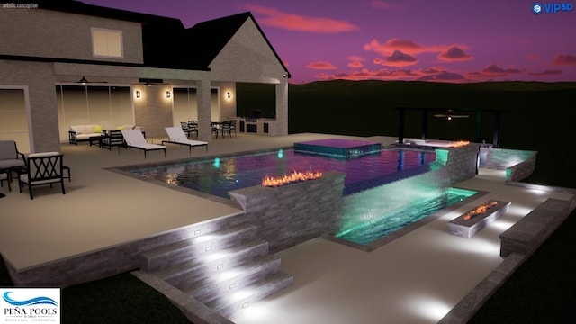 pool at dusk with exterior kitchen, an in ground hot tub, an outdoor living space with a fire pit, a patio area, and a bar