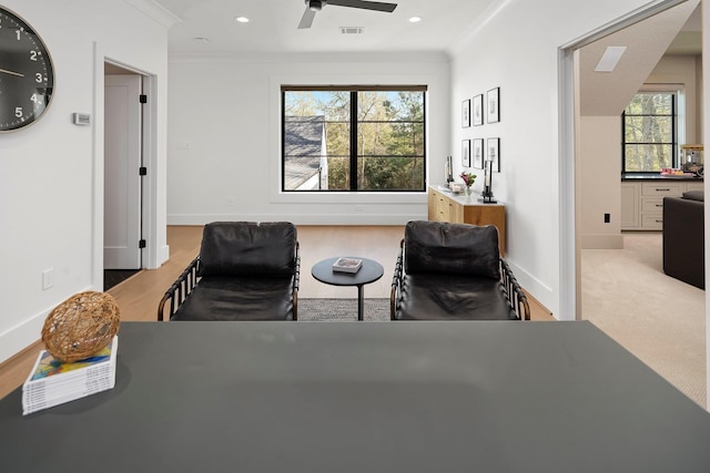 living area with crown molding, ceiling fan, and light colored carpet