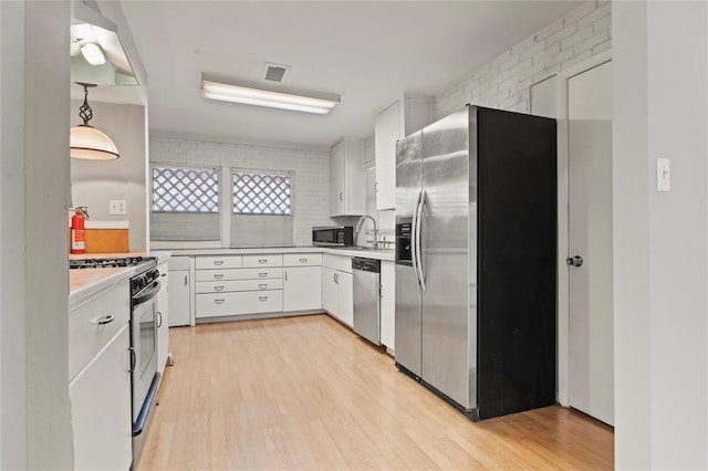 kitchen with light hardwood / wood-style flooring, white cabinets, stainless steel appliances, and decorative light fixtures