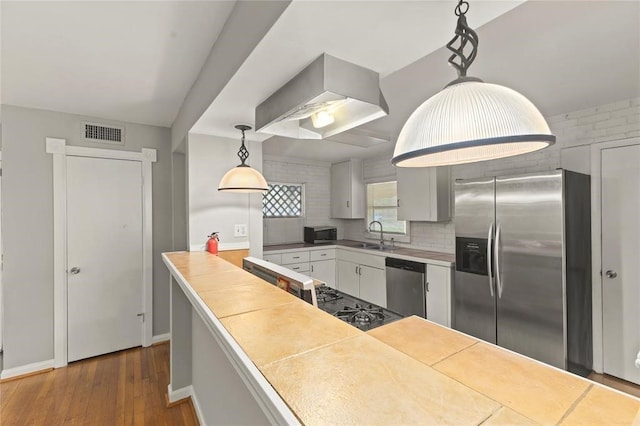 kitchen featuring pendant lighting, white cabinets, dark hardwood / wood-style floors, stainless steel appliances, and brick wall