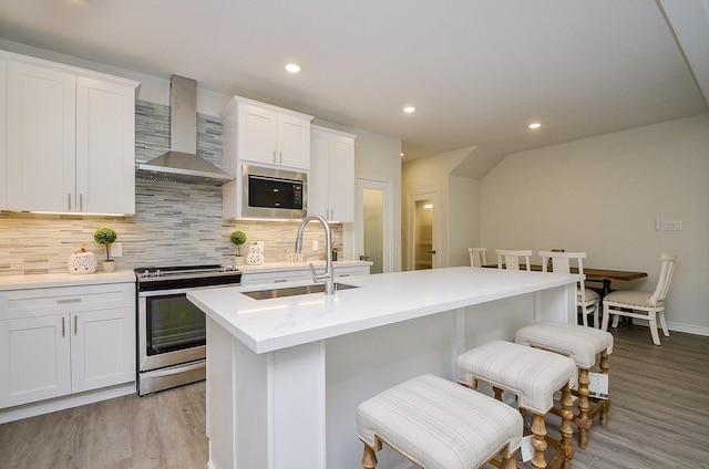 kitchen with sink, stainless steel appliances, wall chimney range hood, white cabinets, and light wood-type flooring