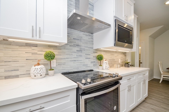 kitchen with decorative backsplash, appliances with stainless steel finishes, wall chimney exhaust hood, light hardwood / wood-style flooring, and white cabinetry