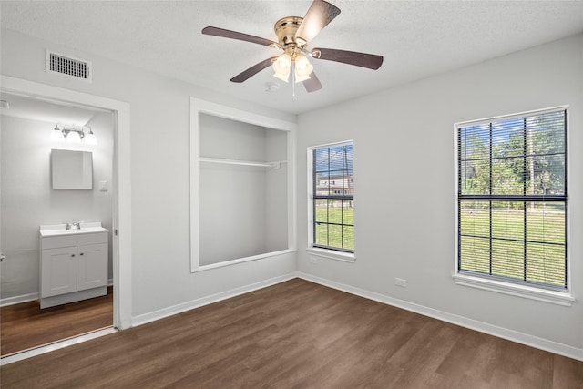 unfurnished bedroom featuring dark hardwood / wood-style flooring, ensuite bathroom, a textured ceiling, ceiling fan, and a closet