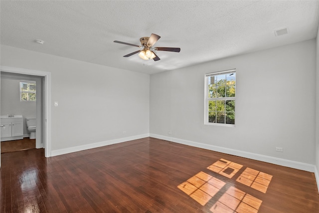 empty room featuring a textured ceiling, plenty of natural light, and dark hardwood / wood-style floors