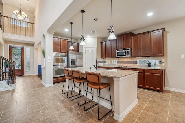 kitchen featuring a kitchen bar, light stone countertops, backsplash, stainless steel appliances, and an island with sink