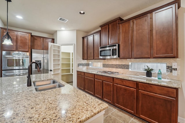 kitchen with light stone countertops, appliances with stainless steel finishes, backsplash, sink, and pendant lighting