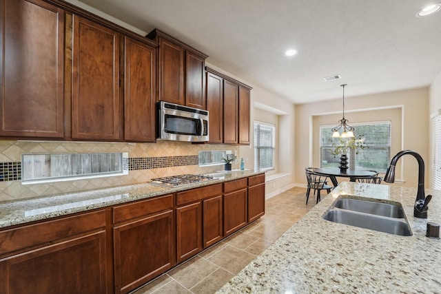 kitchen with backsplash, light stone counters, stainless steel appliances, sink, and a notable chandelier