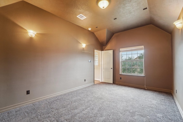 carpeted empty room featuring a textured ceiling and vaulted ceiling