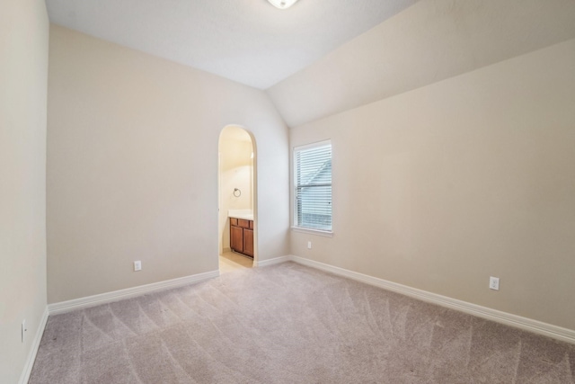 unfurnished bedroom featuring light colored carpet, lofted ceiling, and connected bathroom