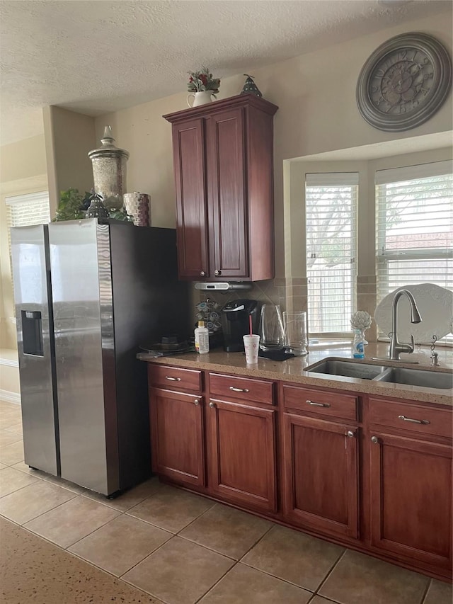 kitchen featuring decorative backsplash, a textured ceiling, sink, light tile patterned floors, and stainless steel fridge with ice dispenser